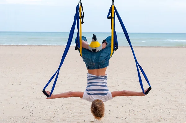 Young woman upside down doing anti-gravity aerial yoga or fly-yoga in hammock on sea background — Stock fotografie