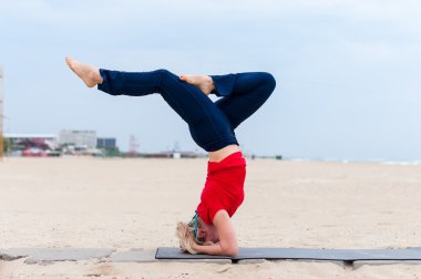 Beautiful young fit woman doing sport exercises, variation of supported headstand posture, salamba sirsasana, side view, coast on gray background
