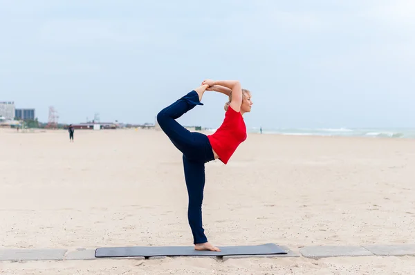 Sporty fit blond woman in red and dark blue sportswear working out outdoors on summer day, doing Natarajasana, Dancer king pose, Dandayamana-Dhanurasana, Standing Bow Bikram posture — Stock Photo, Image