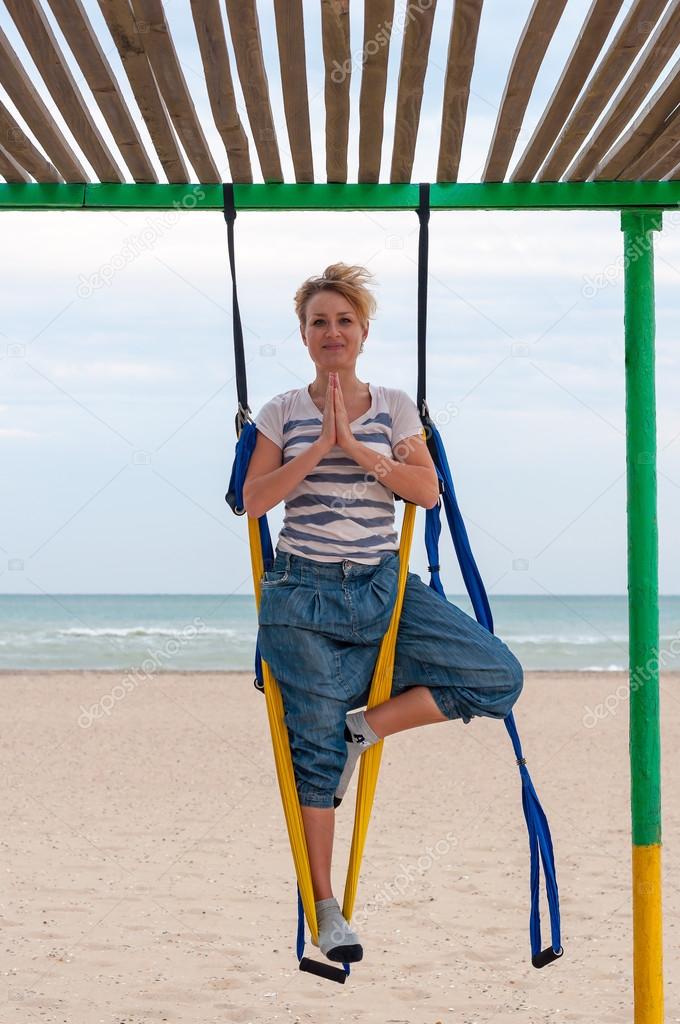 Smiling woman doing anti-gravity aerial yoga on the beach. Fly Yoga in asana, namaste