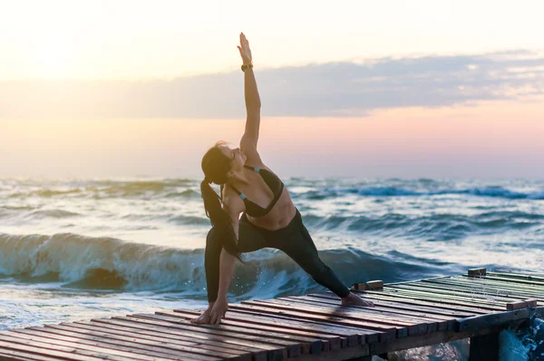 Mladá zdravá žena cvičí jógu na pláži při západu slunce — Stock fotografie