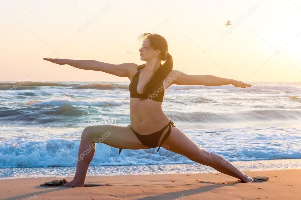 Silhouette of a young woman practicing yoga on the beach at sunrise. Sport, wellness concept