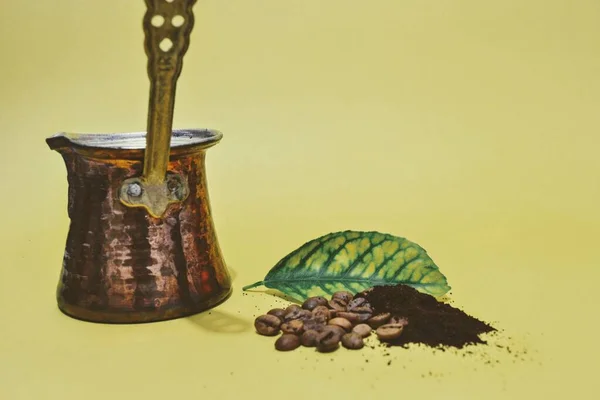 Cooked turkish coffee in traditional pot. coffee beans and roasted-milled coffee with yellow green leaf. Isolated background with yellow background.