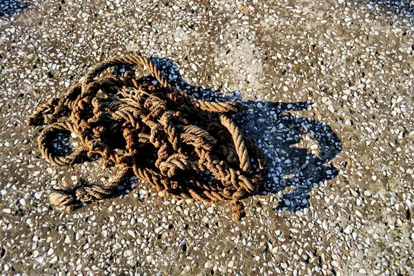 An old and frayed rope standing in a mess. Old rope standing on the concrete floor and its shadow is shown.