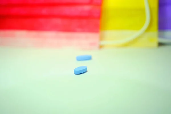 Two piece pills and blue pills with red and yellow colored medical mask background.