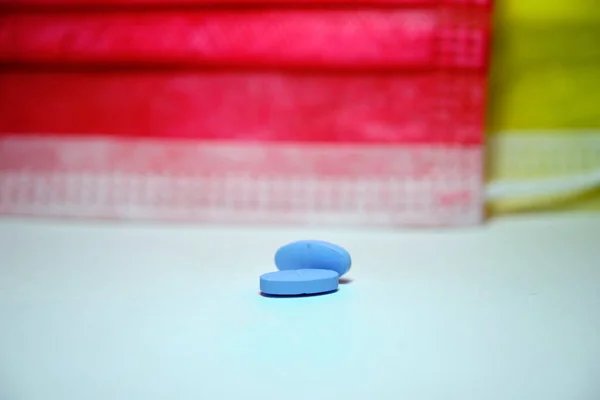 Two piece pills and blue pills with red and yellow colored medical mask background.