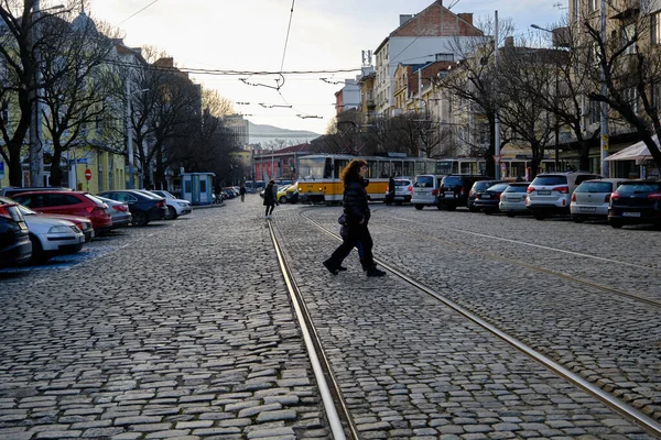 Çarşıya yakın eski sarı tramvay, kaldırım taşının üzerinde kadın çarşısı, etrafta yürüyen insanlar ve caddeye park eden arabalar diye seslendi..