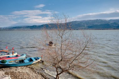 Uluabat Gölü 'nün panoramik manzarası ve güzel gökyüzü ve güneşli bir günde geniş bir dağ arkaplanı. Kıyıda eski ve eski tarz tekneler var. Golyazi. Bursa. Hindi. 22.01.2021.