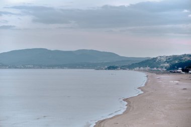 Kumsal, Mudanya 'daki Marmara Denizi kıyısı ve kumsaldaki küçük balıkçı tekneleri, kapalı ve bulutlu havalarda küçük tepe arkaplanmasıyla birlikte..