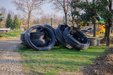 Yerde duran siyah ve plastik borular. Botanik parkında su boşaltma boruları ve oyun alanı geçmişi.