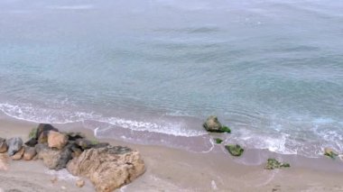 Hava bulutluyken deniz dalgalarının Slow Motion videosu. Turkuaz deniz suları kumsaldaki taşlarla çarpışır..