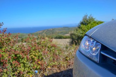 Toprak, yeşil, küçük tepe ve mavi gökyüzü arka planı olan bir arabanın farları..