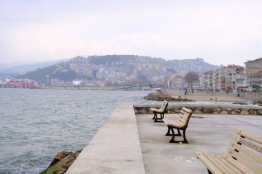 Yağmurlu ve bulutlu havalarda Türkiye 'nin Bursa kentindeki Gzelyal kentindeki ahşap malzemeden yapılmış koltuk bankı. Mudanya Denizi ve deniz kenarında yürüyen kalabalık. 24.02.2021. Bursa. Türkiye.