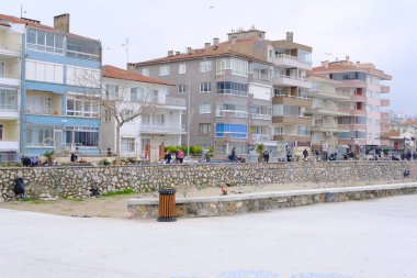 Yağmurlu ve bulutlu havalarda Türkiye 'nin Bursa kentindeki Gzelyal kentindeki ahşap malzemeden yapılmış koltuk bankı. Mudanya Denizi ve deniz kenarında yürüyen kalabalık. 24.02.2021. Bursa. Türkiye.