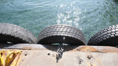 Karaköy İstanbul Boğazı 'nda, turkuaz rengi berrak su renginde bir şeyin yanında duran metal zincir vasıtasıyla asılı eski lastikler.