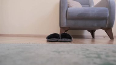 Renkli (kırmızı, beyaz) çoraplar ve kot pantolon giyen genç bir adam. Adam kapalı terlik giyiyor ve ahşap zeminde yürüyor. Bekar ve eski, antika koltuklar, alçak açılı kamera, ahşap zemin ve yeşil halı..