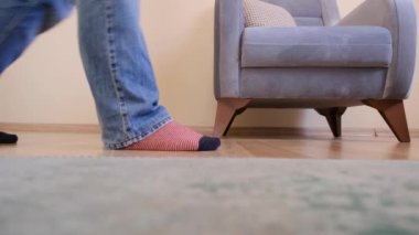 Renkli (kırmızı, beyaz) çoraplar ve kot pantolon giyen genç bir adam. Adam ahşap zeminde volta atıyor. Bekar ve eski, antika, klasik koltuklar ve alçak açılı kamera var olan ahşap zemin ve yeşil halı..