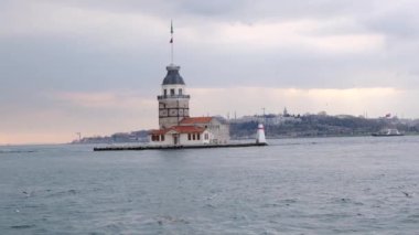 İstanbul, Türkiye 'deki Bakire Kulesi (kiz kulesi), boğaz denizinde güneş ışığının yansımasıyla bulutlu bir havada. Denizde uçan martı grupları. Türkiye 01.03.2021