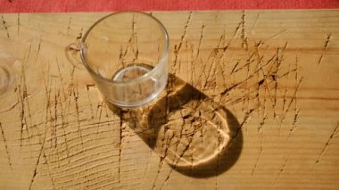 Boş tencere ve bardak cam malzemeden yapılmış. Güneş ışığı altında ahşap bir tabakta ve gölgelerin üzerinde hareket ediyor..