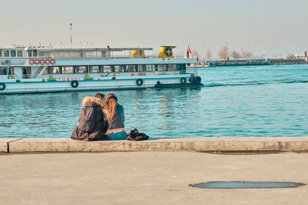 Türkiye istanbul 04.03.2021. Güneşli bir günde Kadıköy 'de birbirine sarılan ve boğaza yaslanan iki genç çift ve sevgili yolcu feribotu ve turkuaz su arka planıyla birlikte..