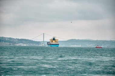 Türkiye istanbul 03.03.2021. İstanbul Boğazı 'ndan geçen büyük bir nakliye gemisi. Bulutlu ve yağmurlu bir günde, küçük bir balıkçı teknesi ve köprü altyapısı var..