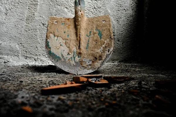 shovel in front of the recently made plastered wall by concrete. green colors exist on metal side of shovel. after construction works. photo taken low angle