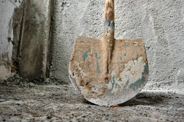 shovel in front of the recently made plastered wall by concrete. green colors exist on metal side of shovel. after construction works. photo taken low angle