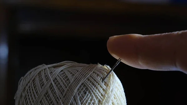 Needle and yellow thread with black background Close up Needle and yellow thread with finger of a man or woman pushing the needle.