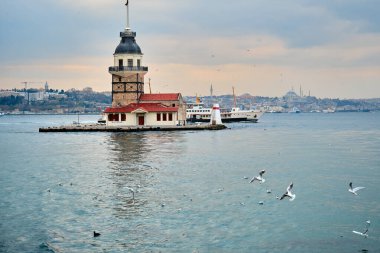 İstanbul, Türkiye 'deki Bakire Kulesi (Kiz kulesi), İstanbul' da hava bulutluyken ve boğaz denizinde güneş ışığı yansıması görülüyorken. Denizde uçan martı grupları. İstanbul Türkiye 01.03.2021