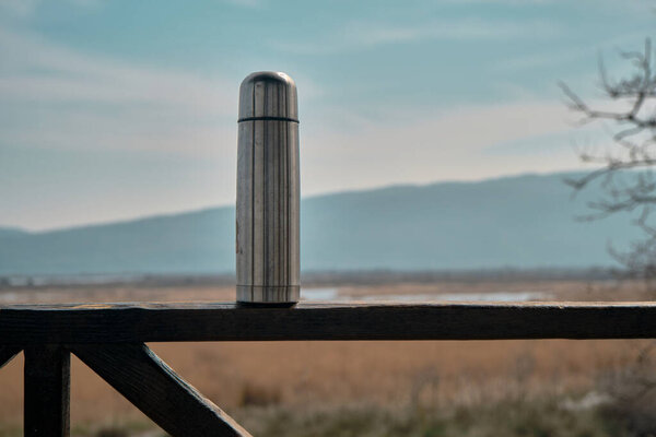 Caffe mug and heat sealing thermos cover made of stainless steel stains on wooden platform by taking photo during trekking in wild nature in forest in karacabey flood plain and huge mountain small.