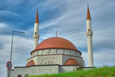İki minare ve kırmızı renkli kubbesi olan yeni kurulmuş camii muhteşem gökyüzü mavi ve bulutlu arkaplan yeşil çimenler ve 4 metre trafik ışığı.