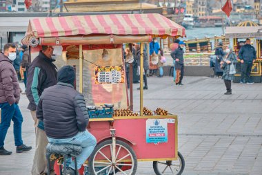 04.03.2021 Türkiye istanbul. İstanbul 'un Eminonu ilçesinde hava bulutluyken sokak mısırları, kestane satıcıları ve antik galata kulesi arka planı ve turist ve yürüyen insanlarla boğaz denizleri vardı.