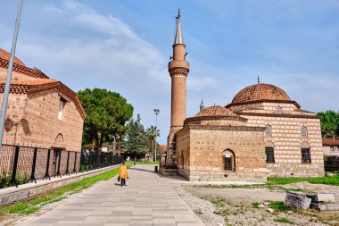 28.04.2021.Nicaea, Bursa Türkiye. Cobblestone yürüyüş yolu ve İznik 'teki İslami Sanat Müzesi ile Şeyh Kutbuddin' in kırmızı tuğlalardan yapılmış oğlu arasında yürüyen sarı elbiseli kadınlarla dolu bir mezar..