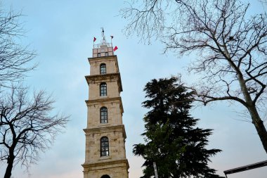 Tophane bölgesindeki Bursa eski gözetleme kulesi solmuş bitki ve ağaç dallarının arkasında gün batımında bulutlu ve yağmurlu arka planda..