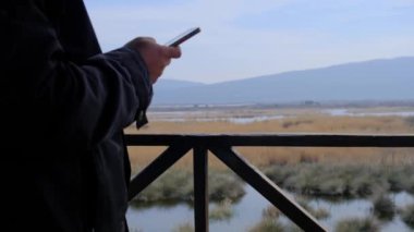 Kuş izleme kulesinde tek bir adam cep telefonuyla kameranın önünde ve karacabey sel ovasının (longoz ormani) arka planında ve bataklık doğası panoramasında oynuyor.