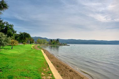 Güneşli bir günde Nicaea 'nın kıyı ve su kıyısında (iznik) ve yakınında küçük patika yolu ve küçük tepe arkaplan ve mavi gökyüzü olan yeşil ağaçlar ve otlarla kaplı bir plaj..