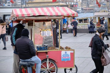 04.03.2021 Türkiye istanbul. İstanbul 'un Eminonu ilçesinde hava bulutluyken sokak mısırları, kestane satıcıları ve antik galata kulesi arka planı ve turist ve yürüyen insanlarla boğaz denizleri vardı.