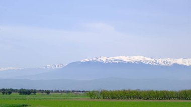 Dağın zirvesinde büyük kar ve mavi gökyüzü arka planında kalır. Küçük orman ve tarım alanı Geliştirilmemiş yol muhteşem büyük dağ (uludag) arka planına sahip yeşil bitkilerle kaplıdır.