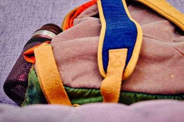 Renkli ve eski tarz sırt çantası ya da tek ve mor renkli koltukta duran sırt çantası. Çantanın paslanmaz çelik bardak tarafı var.