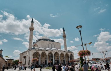 Türkiye 'nin Konya kentindeki Mevlana türbesi yakınlarındaki Sultan Selim Camii (cami) ve güzel ve renkli çiçekler ve mavi ve bulutlu arka planlara sahip çok sayıda insan ve turist. 24.07.2021 Konya. Türkiye