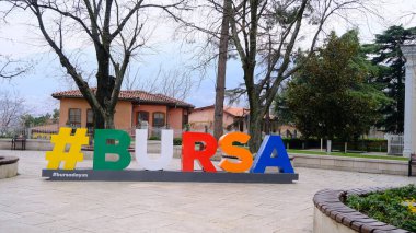 Bursa, Türkiye 29.03.2021. Bulutlu ve bulutlu bir günde hashtag sembollü renkli BURSA ile Bursa tophane Meydanı. Uulu dağı (uludag) arka planına sahip klasik tip kırmızı telpher kabini.