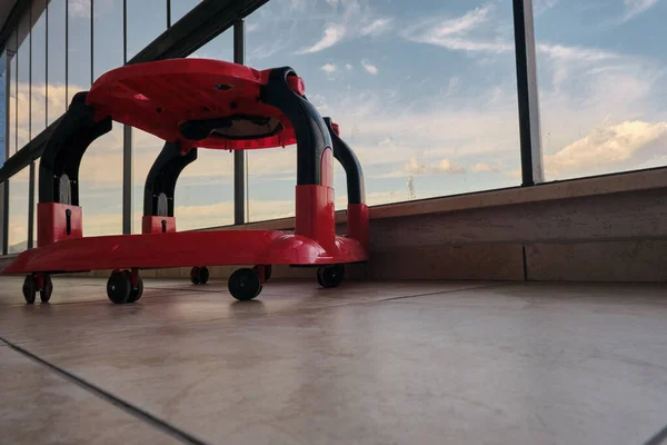 Colorful baby-walker on faience floor inside the huge balcony with cloudy sky background in glass made fences in balcony.