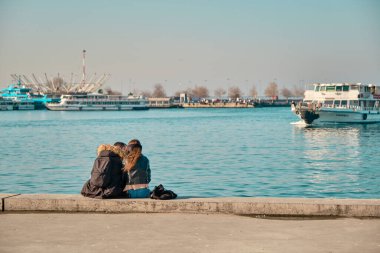 Türkiye istanbul 04.03.2021. Güneşli bir günde Kadıköy 'de birbirine sarılan ve boğaza yaslanan iki genç çift ve sevgili yolcu feribotu ve turkuaz su arka planıyla birlikte..