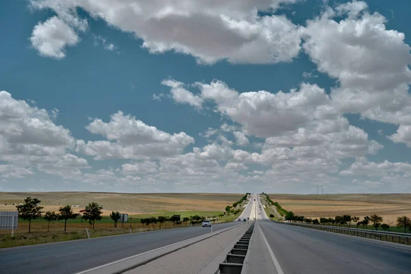 24.07.2021. Konya. Turkey. Straight asphalt way and breakaway barricade with magnificent sky and white clouds and yellow agricultural field on high way