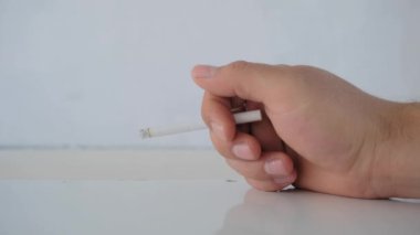 Beyaz ahşap masa üzerinde sigara tutan bir adam ve onun beyaz arka planlı parlak yüzeyi.