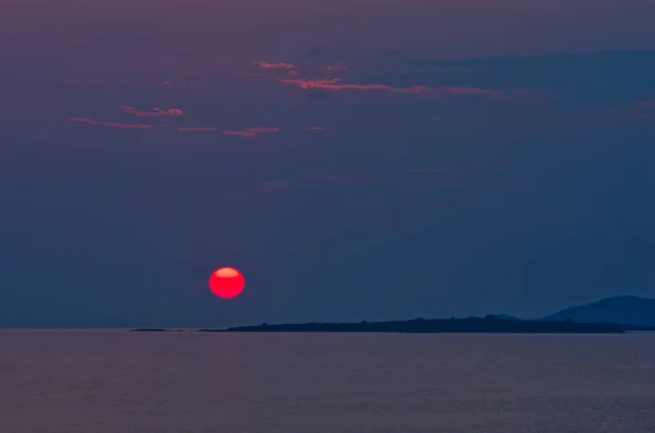 Red sun and sunset at sea below small cape at Sithonia, Greece