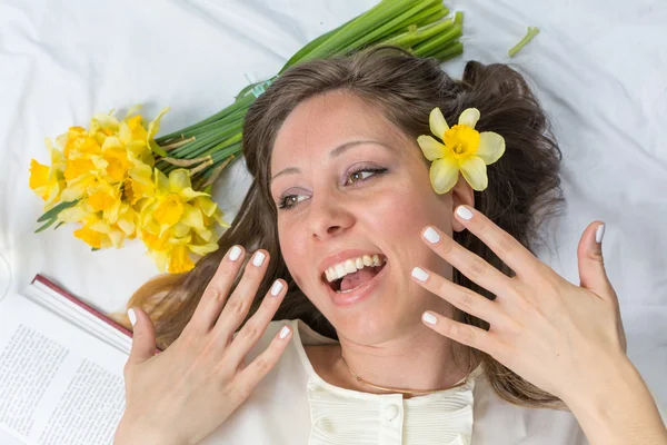 Chica en la cama con narcisos en el pelo — Foto de Stock