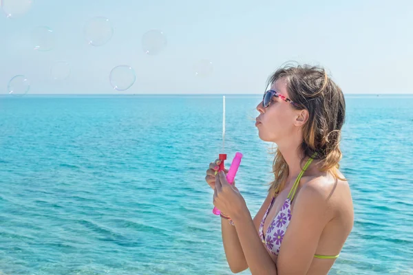 Side portrait of a girl in bikini  blowing soap bubbles at the b — Stock Photo, Image