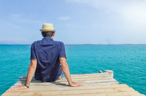 Uomo seduto su un molo in riva al mare — Foto Stock