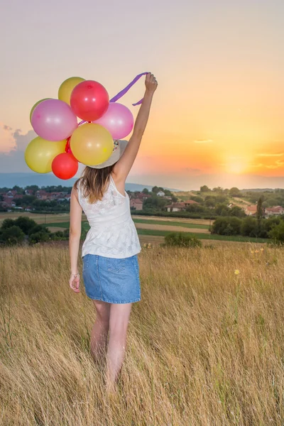 Jovem mulher segurando balões olhando para o pôr do sol — Fotografia de Stock